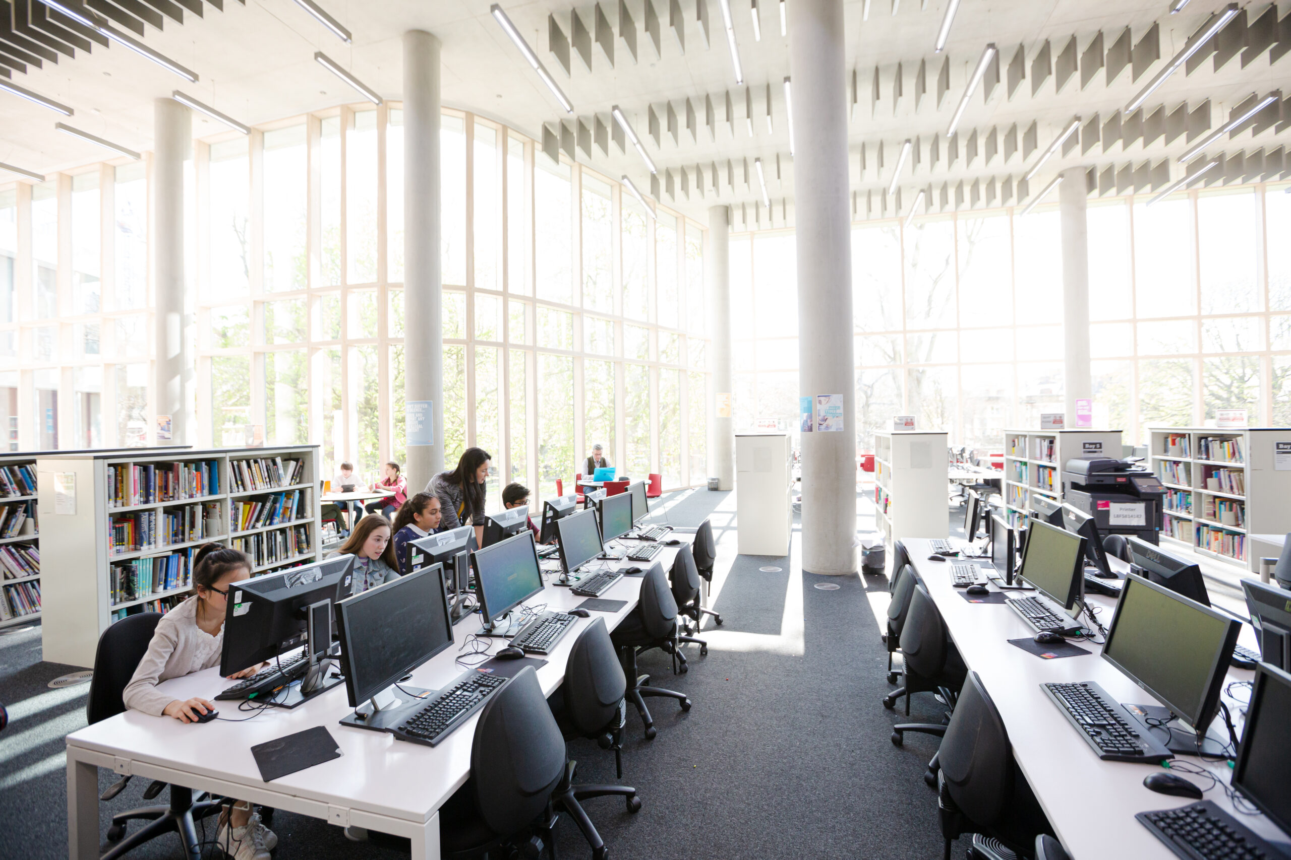 Students working on computers in library with windows and daylight